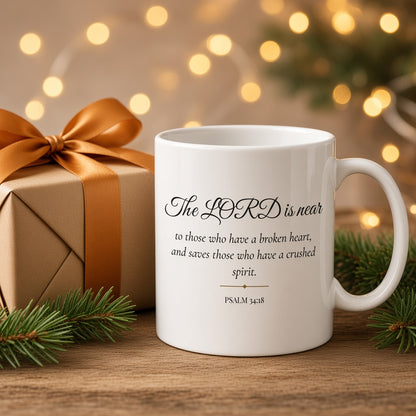 Psalm 34:18 Bible verse mug beside a gift box with Christmas pine and lights